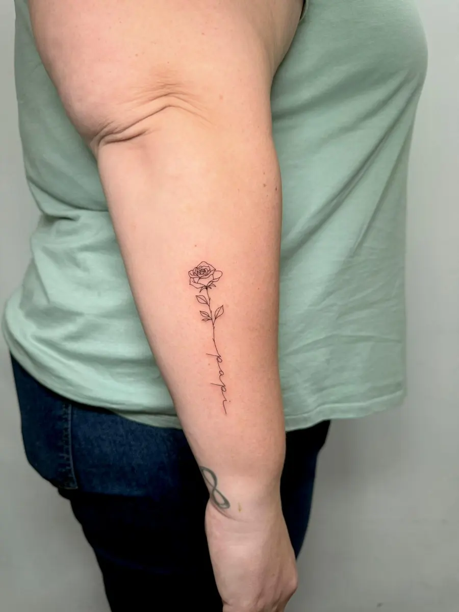 Rose mit vertikalem Schriftzug, Fineline-Tattoo am Oberarm