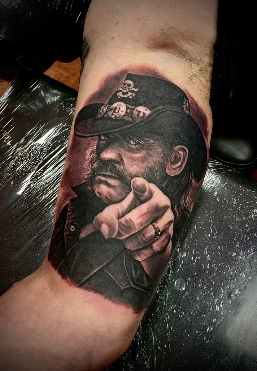 Porträt eines Mannes mit Schirmmütze und erhobenem Finger, Black-and-Grey-Realistic-Tattoo am Unterarm