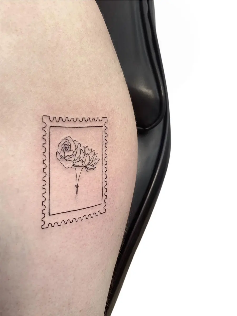 Briefmarken-Motiv mit Blumen, Fineline-Tattoo am Oberarm