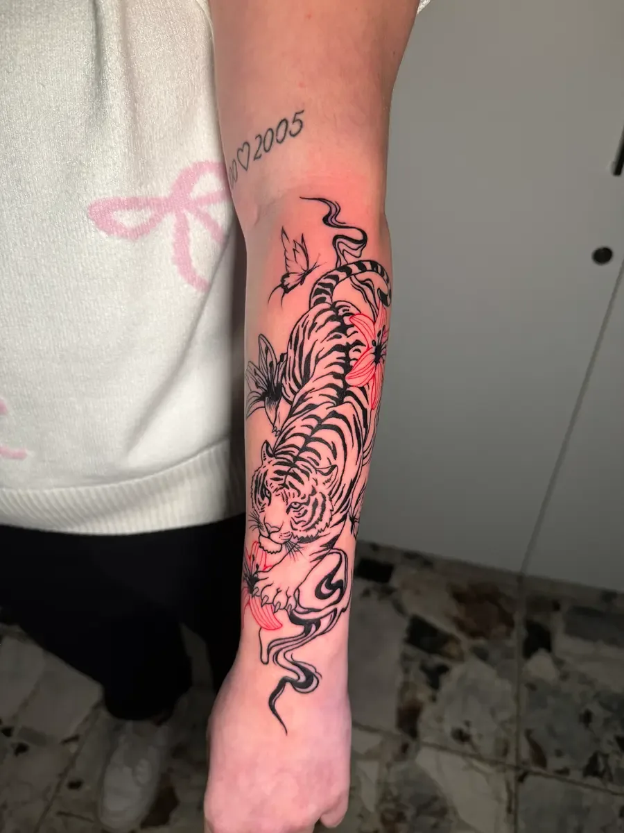 Tiger mit Kirschblüten, Blackwork-Tattoo mit Farbakzenten am Unterarm – Arbeit von Calle, Riverside Ink St. Margrethen
