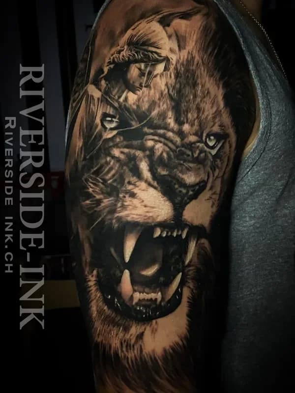 Brüllender Löwenkopf mit Kriegerin, Black-and-Grey-Realistic-Tattoo auf dem Oberarm – Arbeit von Deivson (Dee), Riverside Ink St. Margrethen