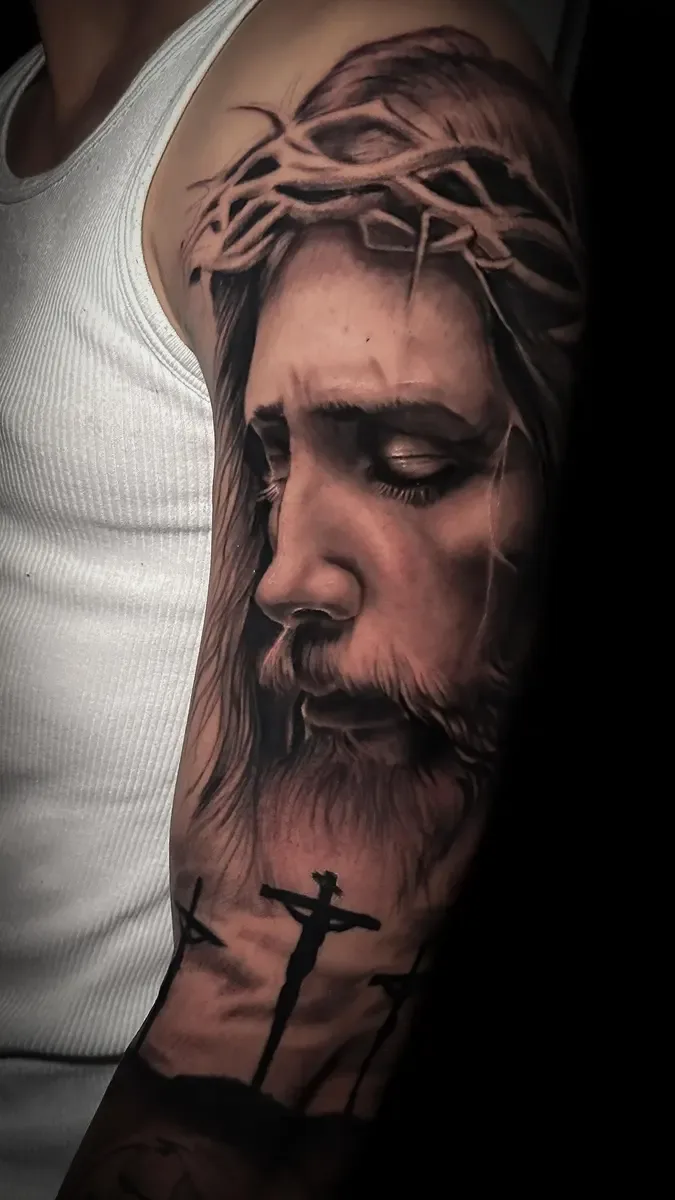 Jesus mit Dornenkrone und Kreuzen, Black-and-Grey-Realistic-Tattoo auf dem Oberarm – Arbeit von Fiser, Riverside Ink St. Margrethen